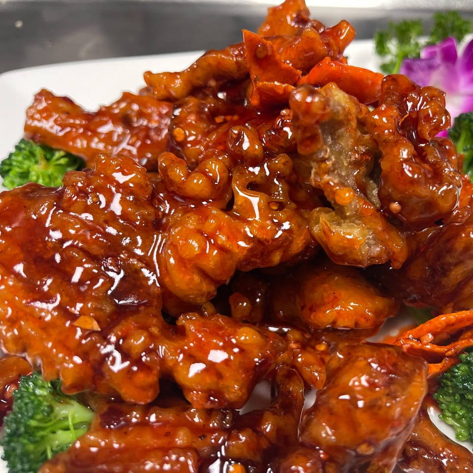 Wild Basil's crispy chicken in a sweet and spicy orange sauce, garnished with broccoli and a purple orchid.
