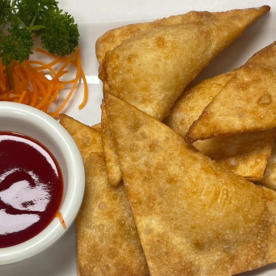 Crispy golden fried wontons with a side of red dipping sauce, garnished with parsley and carrots.