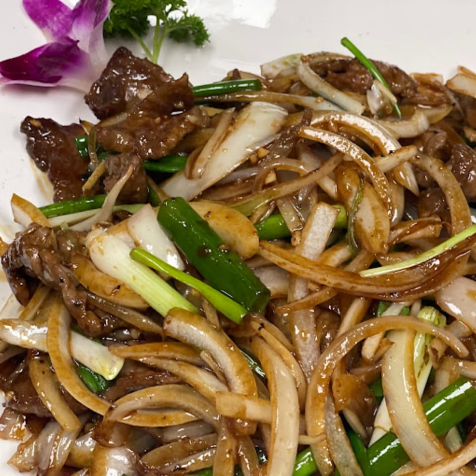 Thai beef and onion stir-fry, garnished with a purple orchid and parsley on a white plate.