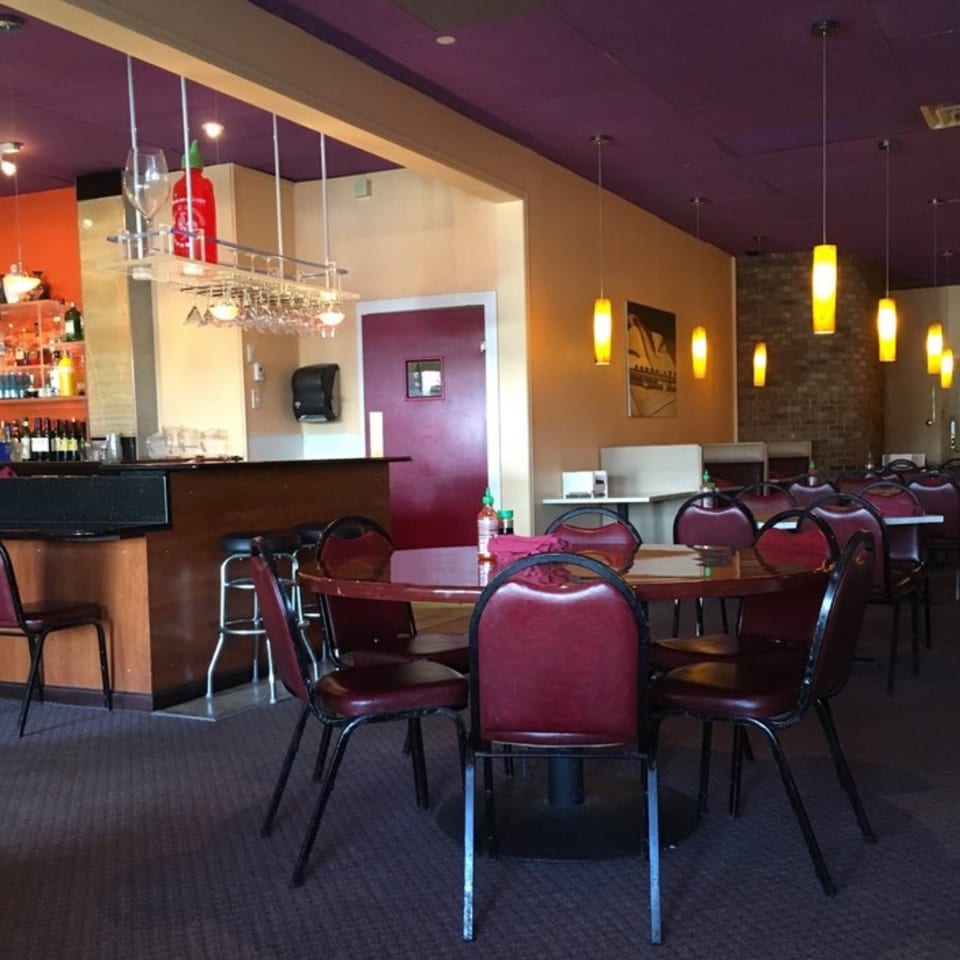 Wild Basil Restaurant's dining area with red chairs, round tables, a bar, and purple ceiling.